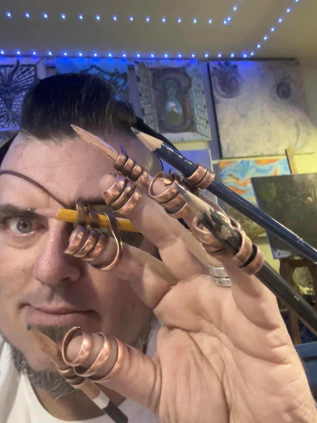 Jesse Montero with copper pencil rigs on his fingers and a pencil held across one eye
